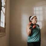 Senior woman in a brightly lit room exercises with dumbbells, promoting fitness at home.