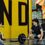 Two young adults in a gym participating in a weightlifting session, sharing a positive moment.