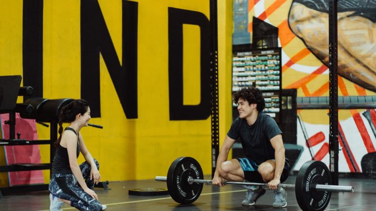 Two young adults in a gym participating in a weightlifting session, sharing a positive moment.